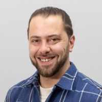 Felix Gundermann - Consultant System Integration: Smiling man with brown beard and brown hair in a braid.