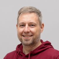 Tobias Klose - Media Designer: Smiling man with grey-blond, short hair and a greyish beard.