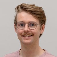 Charles Bailey - UI/UX Designer: Smiling man with red moustache; red wavy hair and thin, round, grey-silver glasses.
